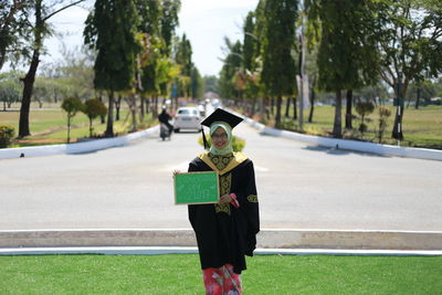 Portrait of woman in graduation gown standing on field