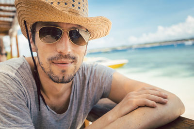 Portrait of mature man wearing sunglasses while sitting by railing against sea