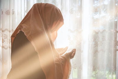 Side view of woman standing against window