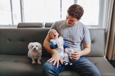 Man sitting with baby boy and dog on sofa in living room at home