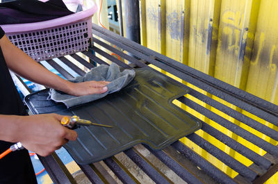 Cropped hands of person cleaning car mat with equipment in garage