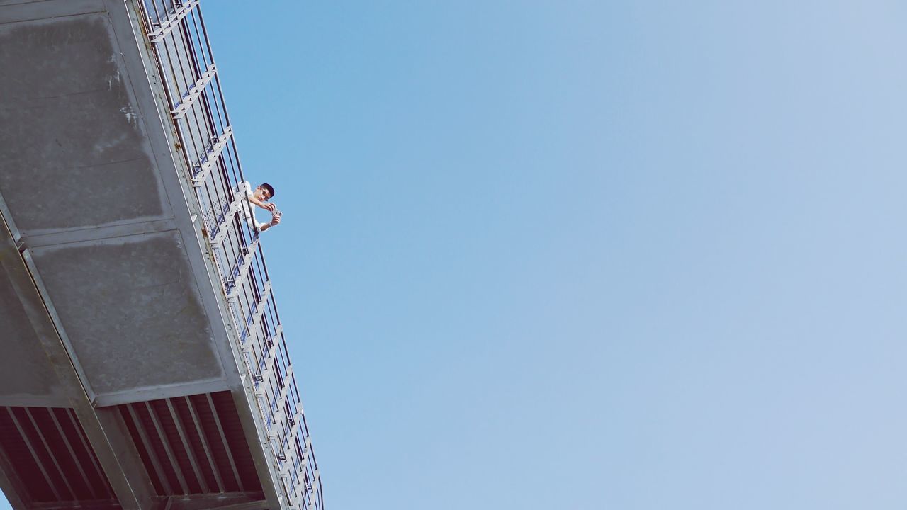 LOW ANGLE VIEW OF MAN WORKING AGAINST BLUE SKY