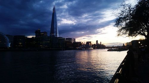 View of buildings by river against cloudy sky