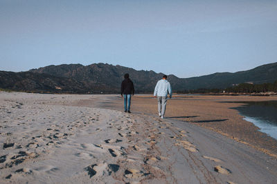 Rear view of man walking at desert against clear sky