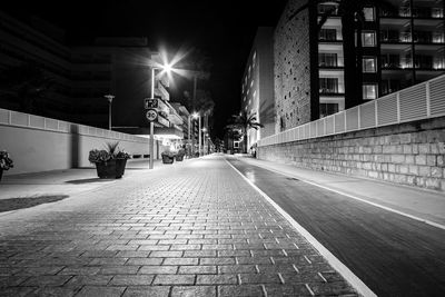 Empty road along illuminated buildings at night