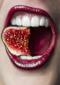 Midsection of woman wearing lipstick while eating fig fruit
