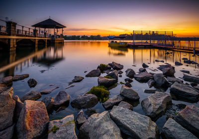 Bridge over river by buildings against sky during sunset