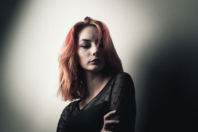 Beautiful young woman looking away while standing against wall