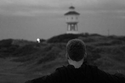 Rear view of man by lighthouse against sky