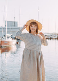 Happy young woman in dress and hat walks on the beach near the boats