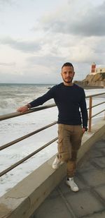 Portrait of young man standing by railing against sea