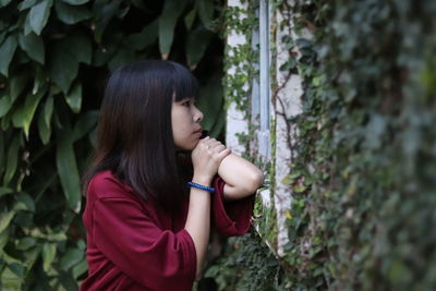 Thoughtful young woman looking away while standing by plants in park