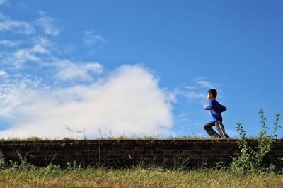 Full length of little boy standing on field against cloudy sky