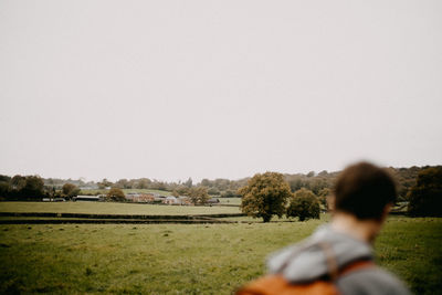 Rear view of man sitting on field against clear sky