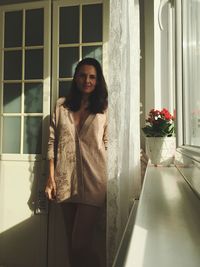 Portrait of smiling young woman standing against window