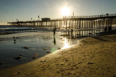 Pier on beach against sky during sunset