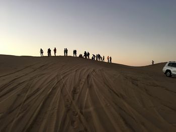 People on desert against sky during sunset