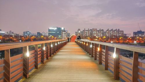 Illuminated bridge and buildings against sky in city