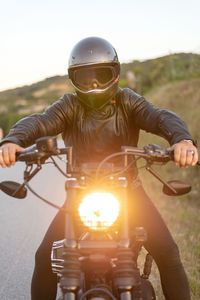 Biker in helmet sitting and relaxing on vintage motorcycle on sunset.