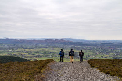 Rear view of people walking on mountain against sky