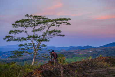 Photographer standing by tree against sky during sunset