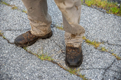 A man in splattered work boots and pants on broken asphalt street