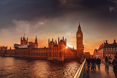 People walking on bridge against big ben in city during sunset