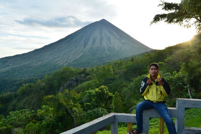 Man sitting on mountain against sky