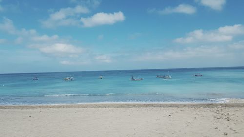 Boats in calm blue sea against cloudy sky