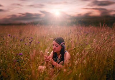 Young woman with purple flowers on field during sunset
