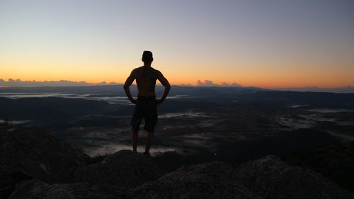 Man standing on rock against sky during sunset