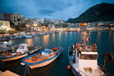 Boats moored at harbor by buildings in city against sky