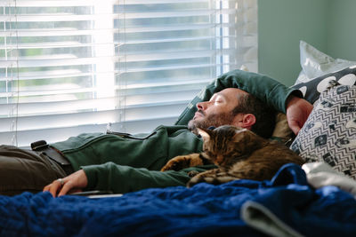 Man takes a cat nap with his tabby cat snuggling next to him