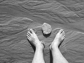 Low section of man standing on wet sand at beach