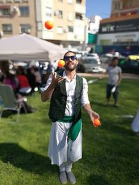 Full length of young man wearing sunglasses juggling balls while standing on grassy field