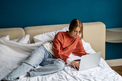 Young woman using laptop while lying on bed at home