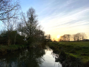 Canal amidst trees against sky during sunset