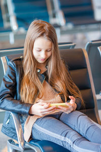 Girl using mobile phone while sitting at airport