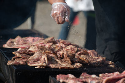 Midsection of person sprinkling spice over meat cooking on barbecue grill