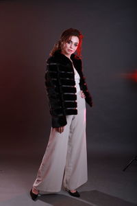 Fashionable young woman wearing fur jacket while standing against gray background