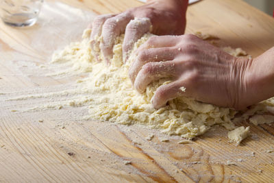 Cropped hands kneading dough on wooden table at home