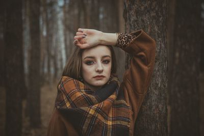 Portrait of woman standing against tree trunk