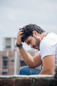 Young man with looking away while sitting against building