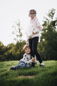 Full length of happy friends sitting on grass against plants