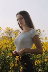 Thoughtful young woman looking down while standing by yellow flowering plants at farm