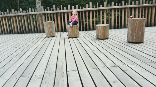 Baby girl sitting on tree stump at boardwalk