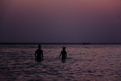 Silhouette couple enjoying in sea against clear sky during sunset