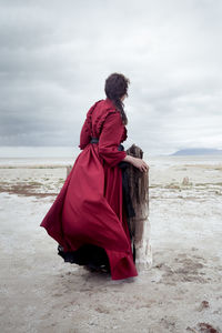 Rear view of woman standing at beach against sky