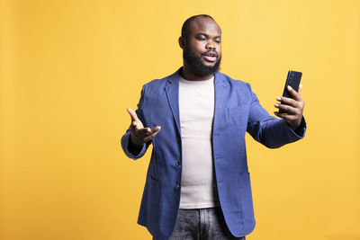 Young man using mobile phone against yellow background