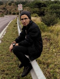 Portrait of young man sitting on railing at roadside